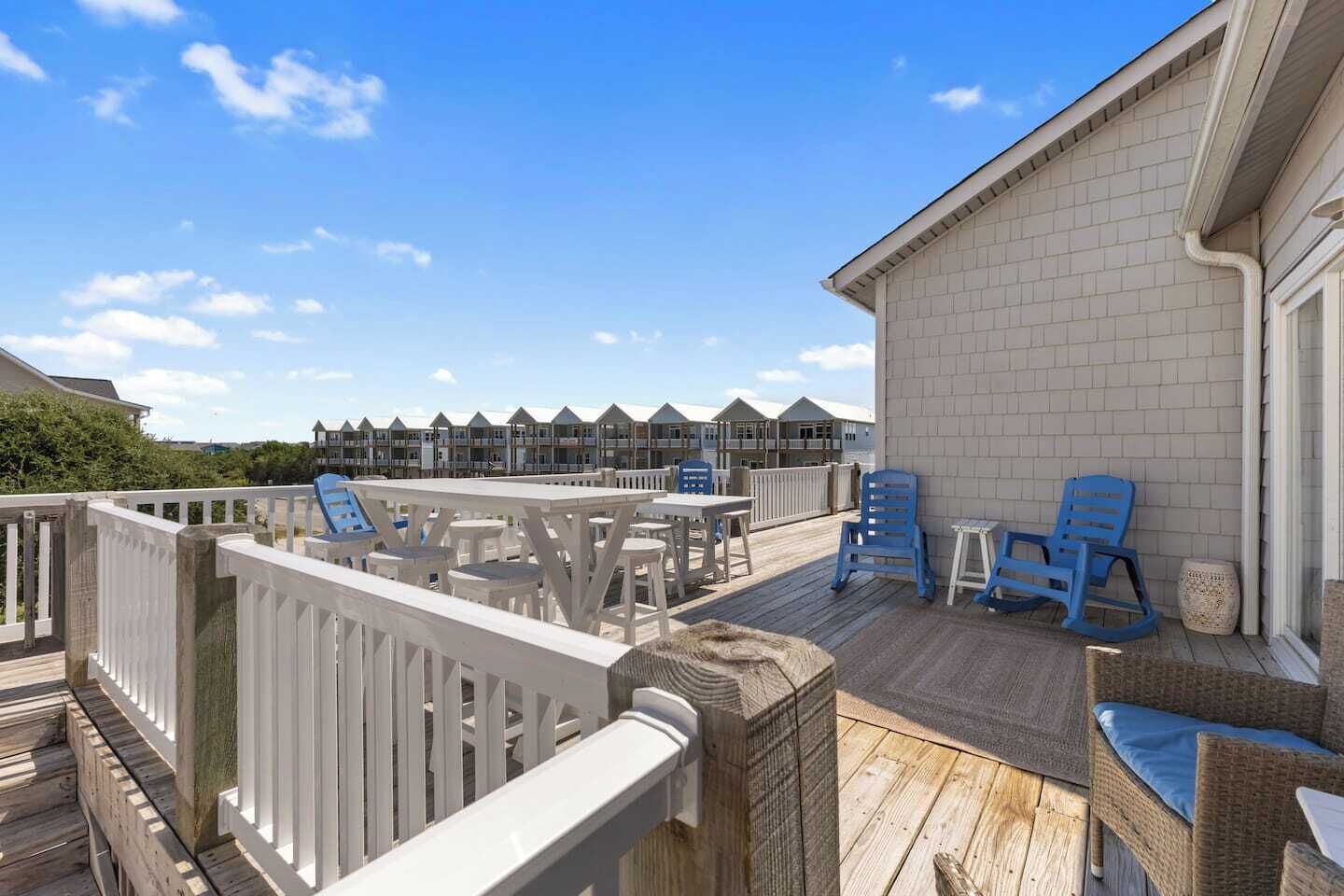 A wooden deck with white railings, blue chairs, and a table.