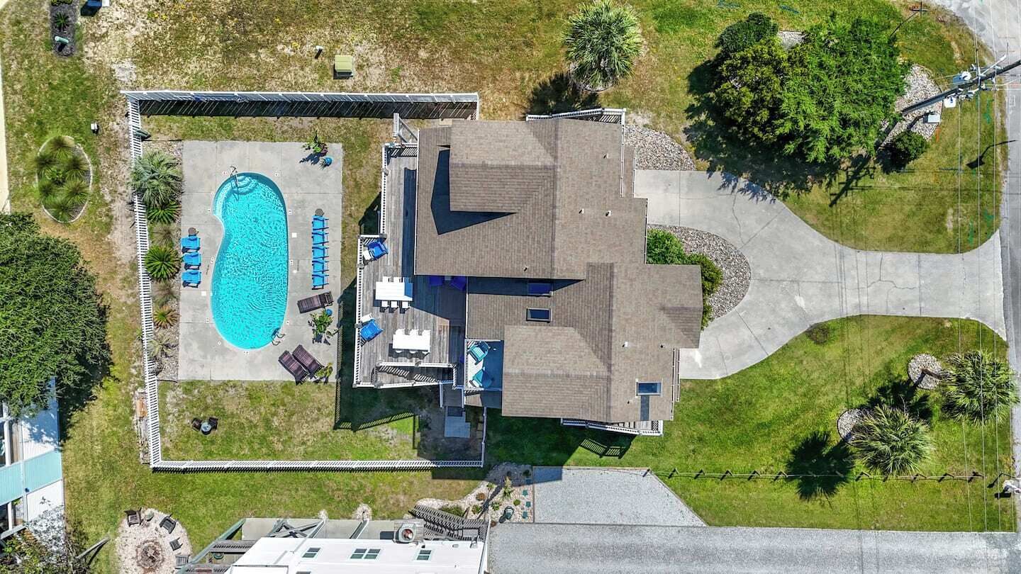 An aerial view of a property with a swimming pool, a covered patio, and a large building with a sloped roof.