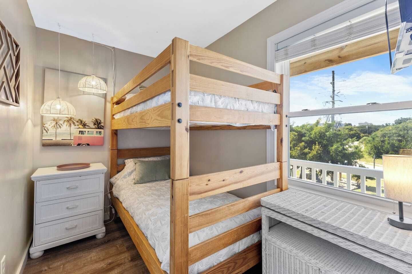 Una cama individual con escritorio y cómoda, una lámpara colgante, y una ventana con vistas a la vegetación.