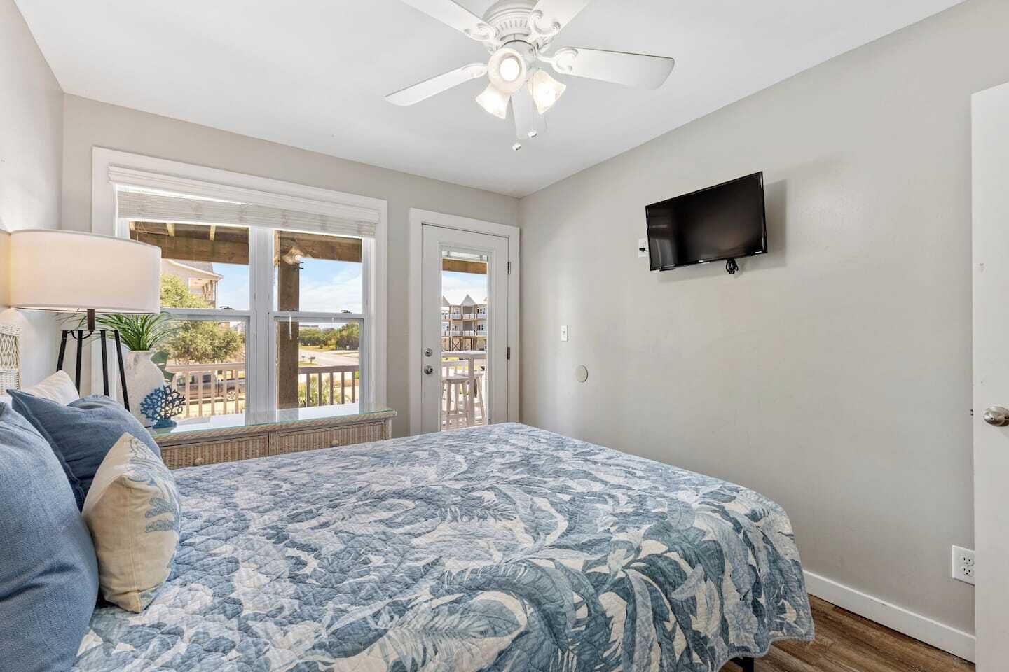 A bedroom with a bed, a ceiling fan, a TV, and a window with a view.