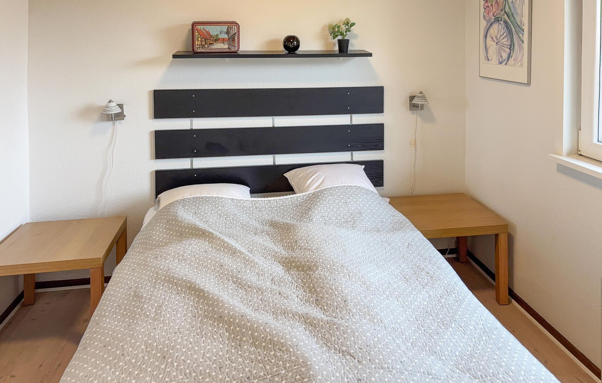 Une chambre à coucher comprenant un lit, deux tables de chevet, une tête de lit, une étagère murale décorative et une fenêtre.