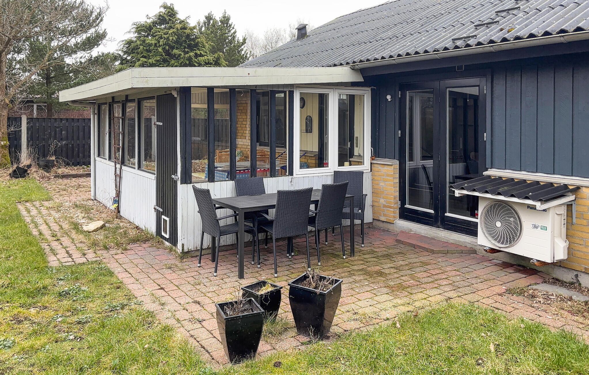 En overdækket terrasse med bord, stole, ventilator og plantekasser.