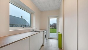 Une petite cuisine avec une fenêtre, un lave-linge et une poubelle verte.