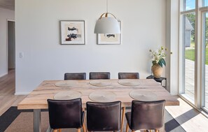 Ein Esszimmer mit Holztisch, schwarzen Stühlen, einer hängenden Leuchte und zwei gerahmten Kunstwerken an der Wand.
