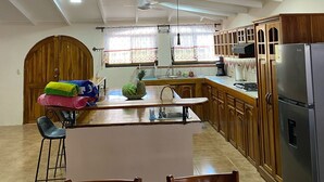 Une cuisine dotée d’un îlot central, de meubles en bois, d’un ventilateur de plafond et d’un réfrigérateur.