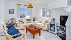 Ein modernes Wohnzimmer mit einer Sofagarnitur, einem Holztisch, einem Sessel, einer TV-Konsole und einem großen Fenster mit Blick.