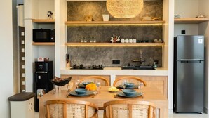 A compact kitchen with built-in appliances, a dining table with chairs, and a hanging light fixture. - Mountain Sunshine Private Villa (Sukawati)