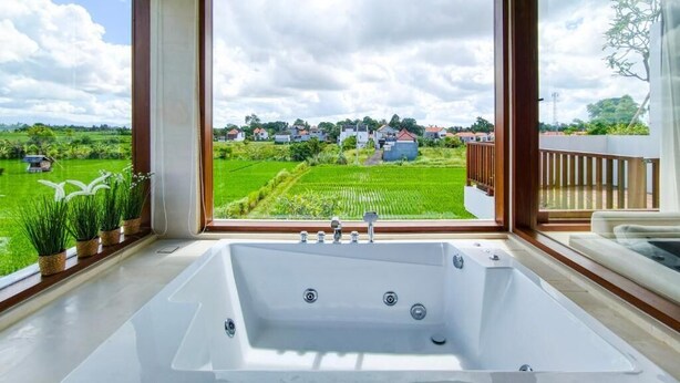 A large bathroom with a bathtub, a view of a green landscape, and a balcony with a wooden railing. - Mountain Sunshine Private Villa (Sukawati)