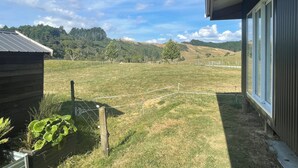 A view from a house's porch overlooking a grassy field with a wooden structure and a metal fence.
