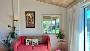 A room with a red sofa, a framed picture on the wall, a window with curtains, and a potted plant.