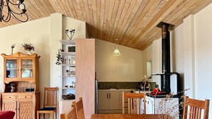 A wooden dining table with chairs, a cabinet with glass doors, a hanging light fixture, and a kitchen area with a stove.