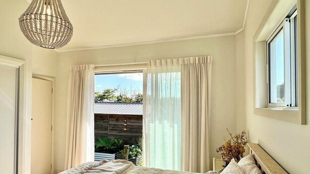 A bedroom with a bed, a bedside table, a lamp, a window, and a view of the outdoors.