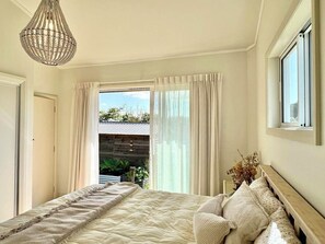 Un dormitorio con cama, mesita de noche, lámpara, ventana y vistas al exterior.