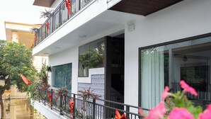 A multi-story building with balconies adorned with red bows, large windows, and a garden area with potted plants. - Chu Homestay TamCoc (Nam Hoa Lu)