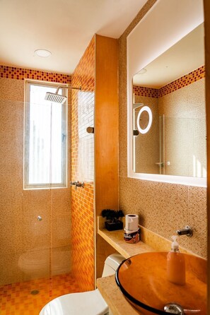 Un baño con ducha, inodoro, lavamanos con espejo y un perchero para toallas.