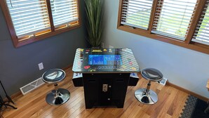 A room with a gaming table, two stools, and a large window with blinds.