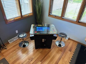 A room with a gaming table, two stools, and a large window with blinds.