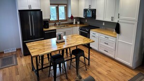A modern kitchen with white cabinets, a black refrigerator, a wooden dining table, and a black stove.