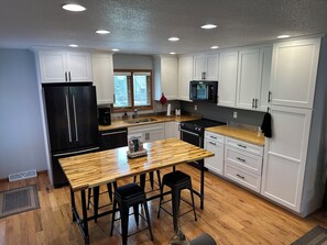A modern kitchen with white cabinets, a black refrigerator, a wooden dining table, and a black stove.