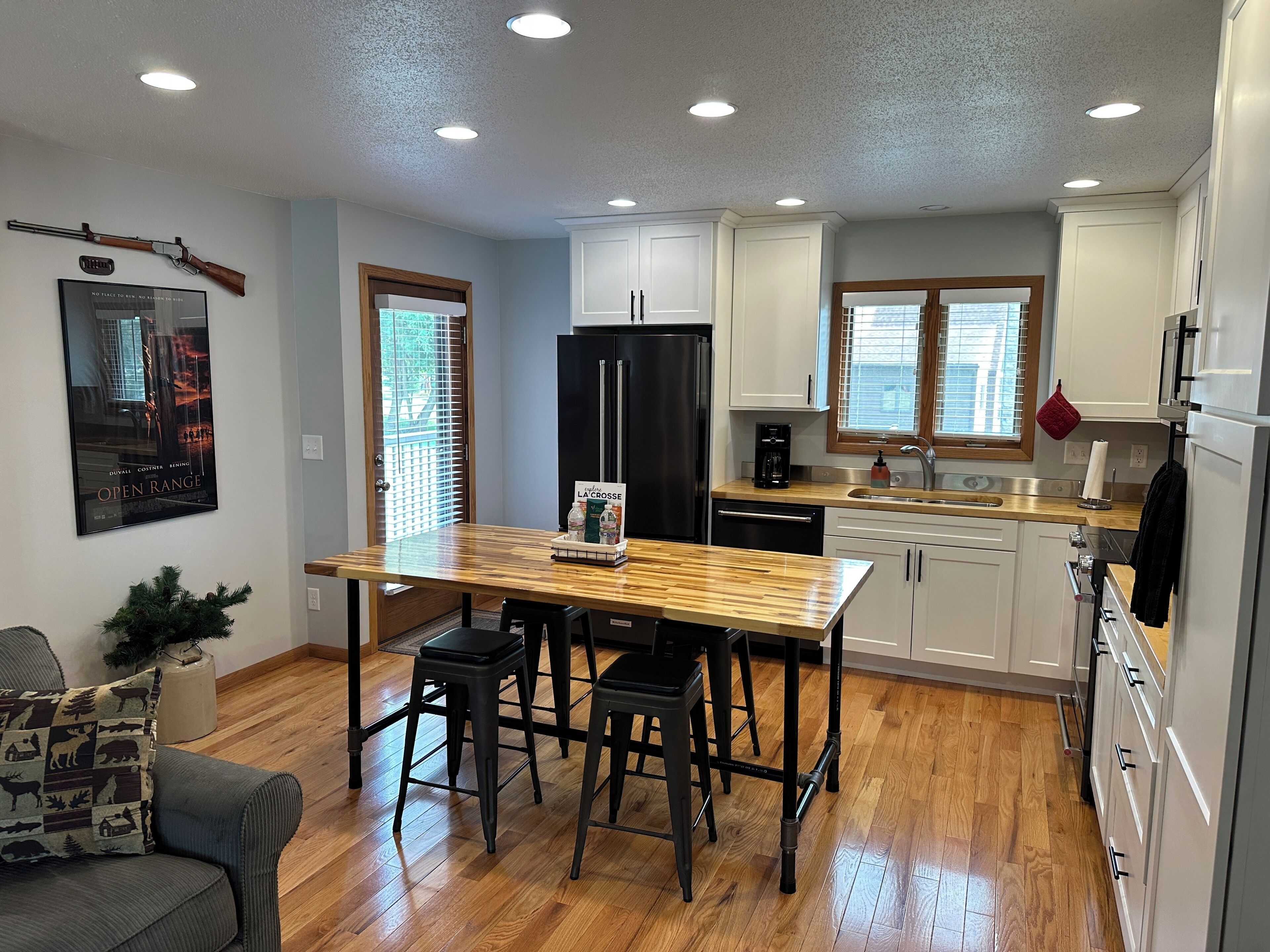 A modern kitchen with white cabinets, a black refrigerator, and a wooden dining table.
