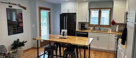 A modern kitchen with white cabinets, a black refrigerator, and a wooden dining table.