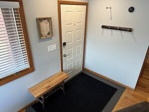 A hallway with a wooden bench, a door, a wall-mounted light fixture, and a framed informational sign. - Cozy Hillside Hideaway (La Crosse)