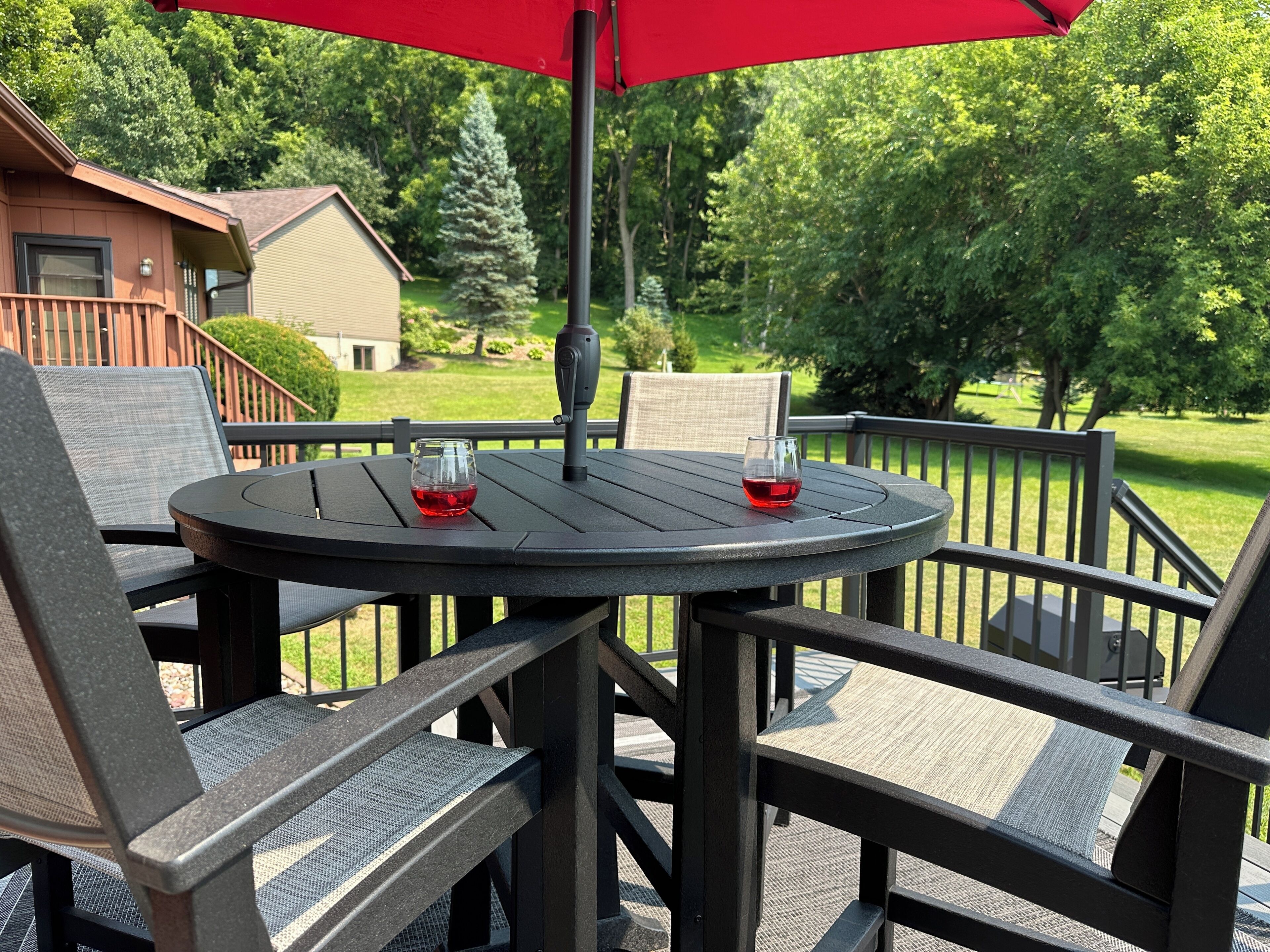 An outdoor patio with a round table, two chairs, and a red umbrella.