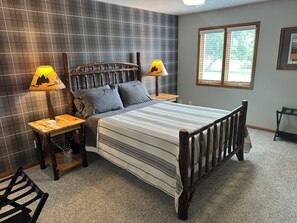 A bedroom with a bed, two nightstands, a lamp, a window, and a wall with a grid pattern. - Cozy Hillside Hideaway (La Crosse)