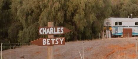 Ein Wegweiser zeigt die Richtung nach Charles und Betsy, ein Oldtimerbus und ein eingezäunter Bereich mit vereinzelter Vegetation.