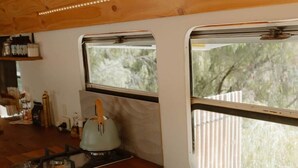 A compact kitchen with a gas stove, a kettle, and a window with a view of trees. - R&R Bus Retreat: Charles the white Bus (Wellington Mill)