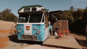 Un autobus bleu et blanc doté d’une rampe menant à une terrasse en bois.