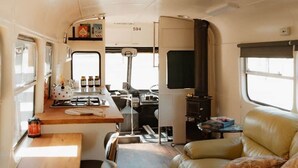 Un intérieur de camping-car compact comprenant un coin cuisine, un espace repas, un coin salon avec un canapé et un téléviseur fixé au mur.