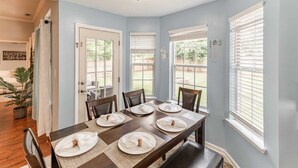 A dining area with a table set for six, a light blue wall, and a view of the backyard.