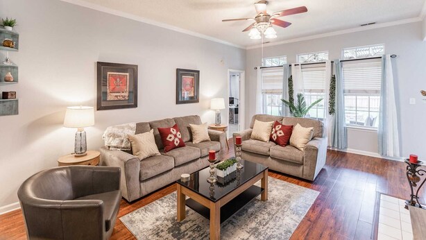 A living room with two sofas, a coffee table, a ceiling fan, and a view of the outdoors through large windows.