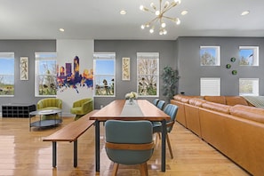 Ein modernes Wohnzimmer mit einem Holzesstisch, grün- und blaue Stühle, ein braunes Ledersofa und große Fenster mit Blick auf die Stadt.