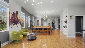 Uma sala de estar ampla com piso de madeira, uma mesa de jantar e duas poltronas verdes.