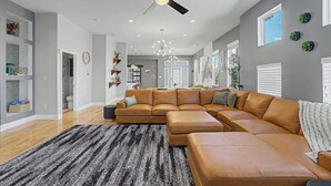 Uma sala de estar ampla com sofá modular, ventilador de teto, iluminação embutida e uma janela grande.
