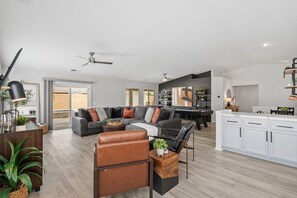 Ein modernes Wohnzimmer mit einer Eckcouch, einem Couchtisch und einem Essbereich, im Hintergrund ist eine Küche zu sehen.