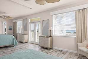 Ein Schlafzimmer mit Bett, Schminktisch, Lampe und großen Fenstern mit Jalousien.