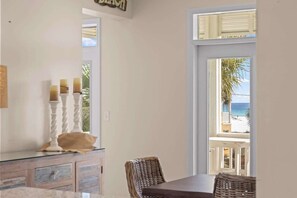 Ein Zimmer mit Esstisch, Korbstühlen, einer Konsolentisch mit Glasplatte und Blick auf den Strand.