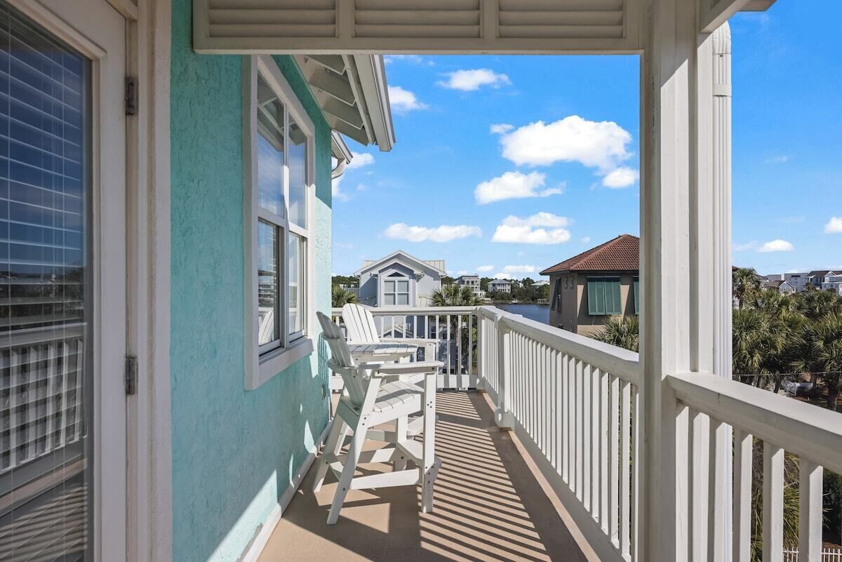 A balcony with white railings, a chair, and a view of neighboring houses.