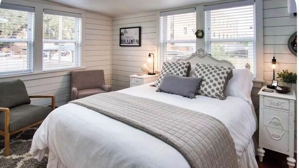 Quarto com cama, cadeira, mesa de cabeceira e janela.