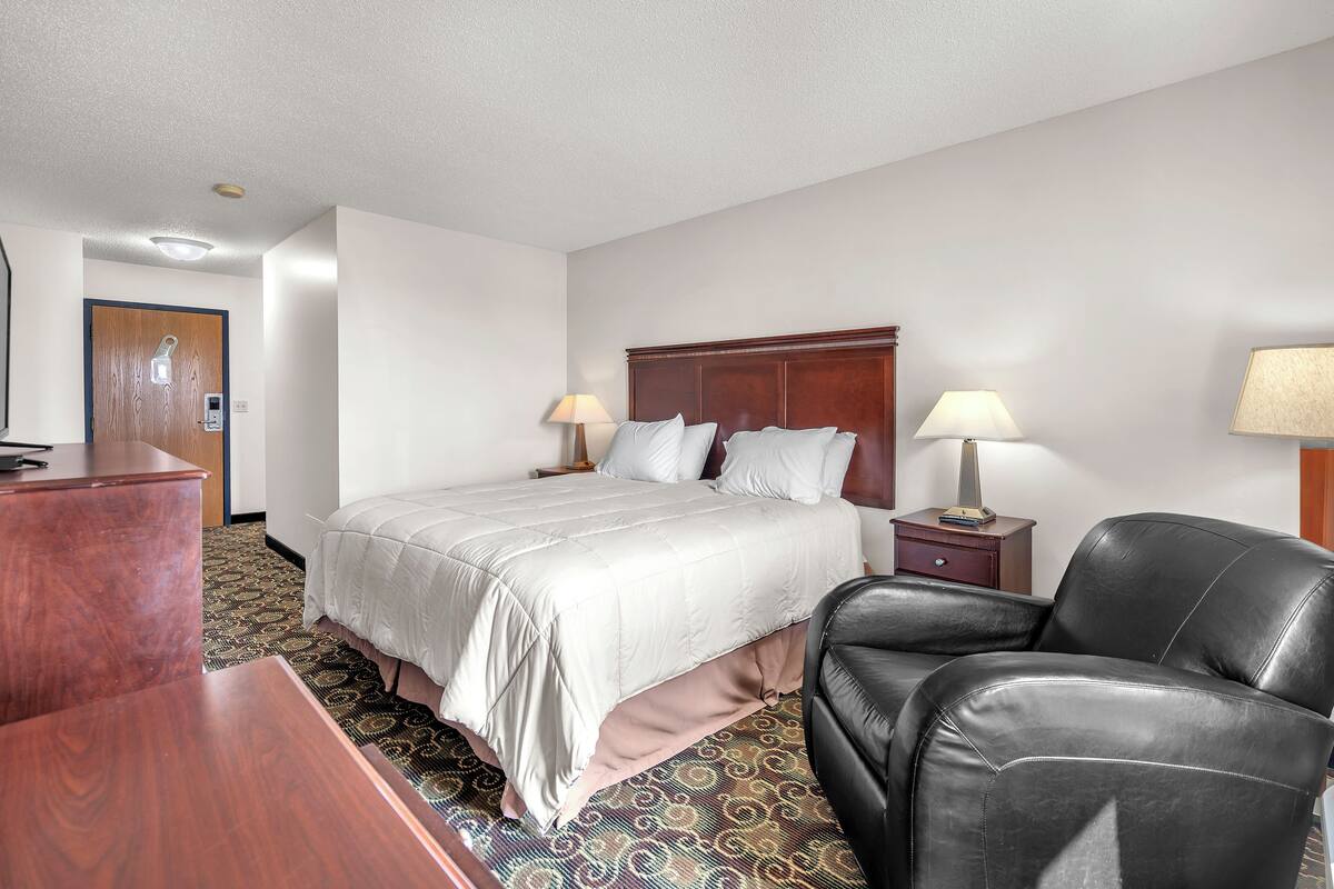A hotel room with a bed, two bedside tables, a desk, a chair, and a patterned carpet.