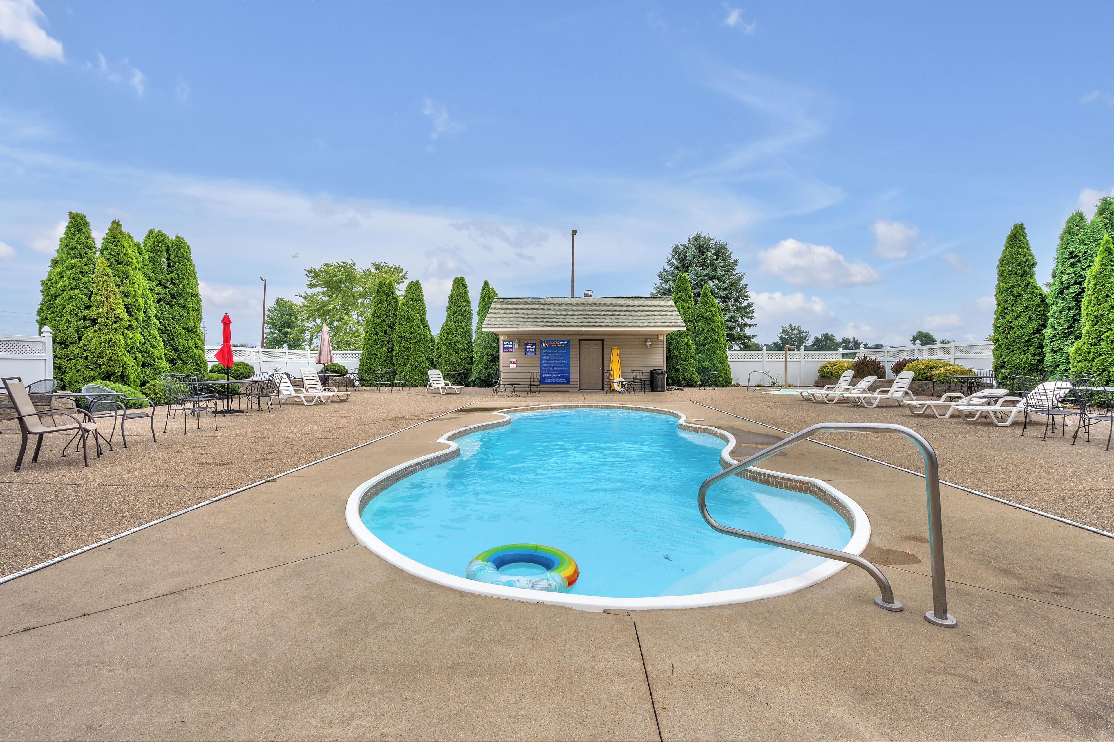A swimming pool with a lifeguard tower, lounge chairs, and a small building in the background.