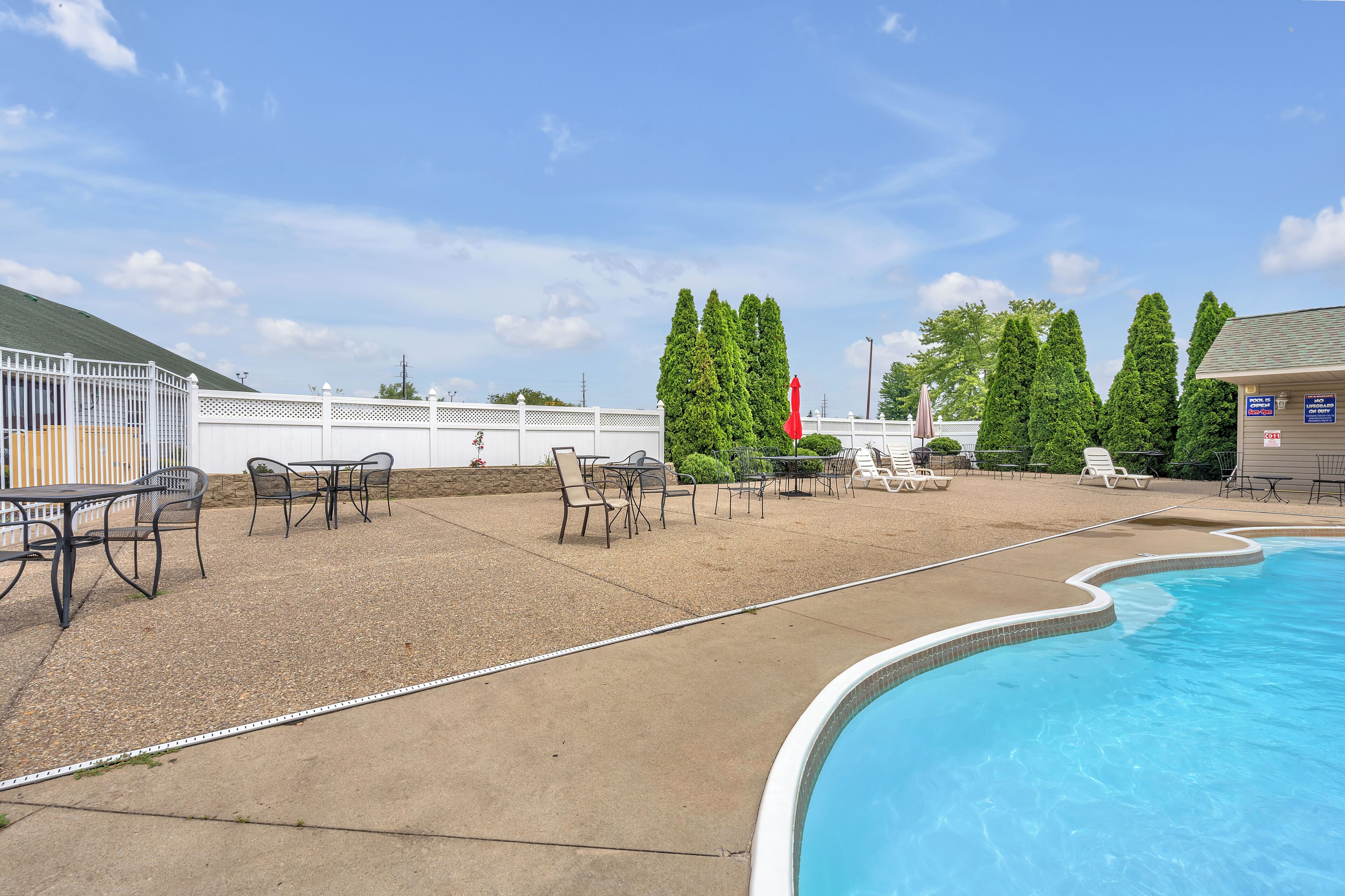 A swimming pool with lounge chairs and tables, surrounded by a white fence and trees.