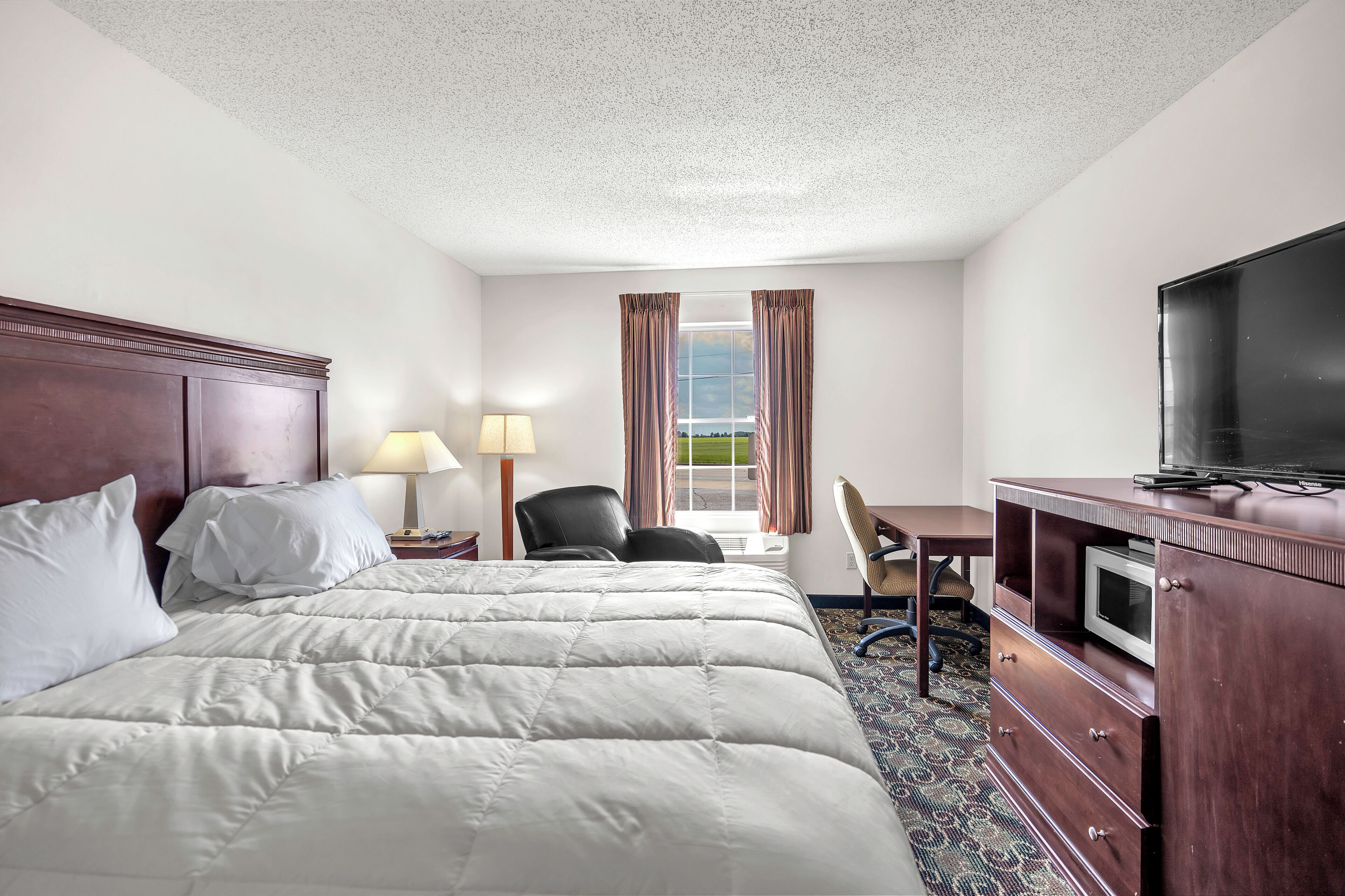 A hotel room with a large bed, a TV, a desk, and a window with curtains.