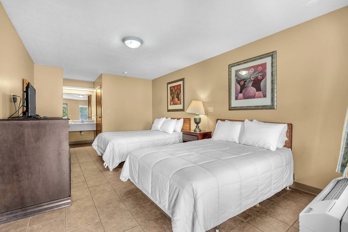 A hotel room with two beds, a desk, a lamp, and artwork on the walls.