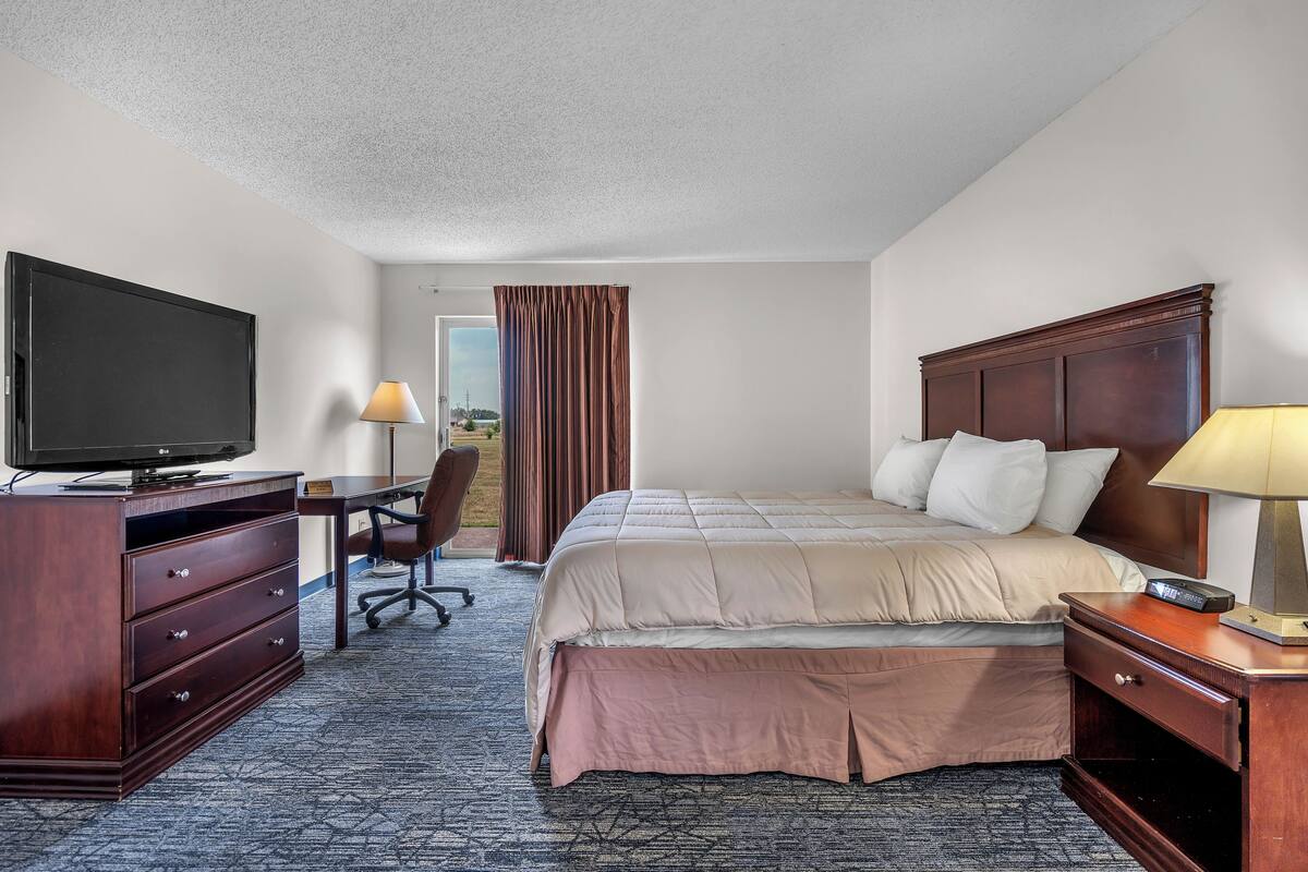 A hotel room with a bed, desk, TV, and a view through the window.