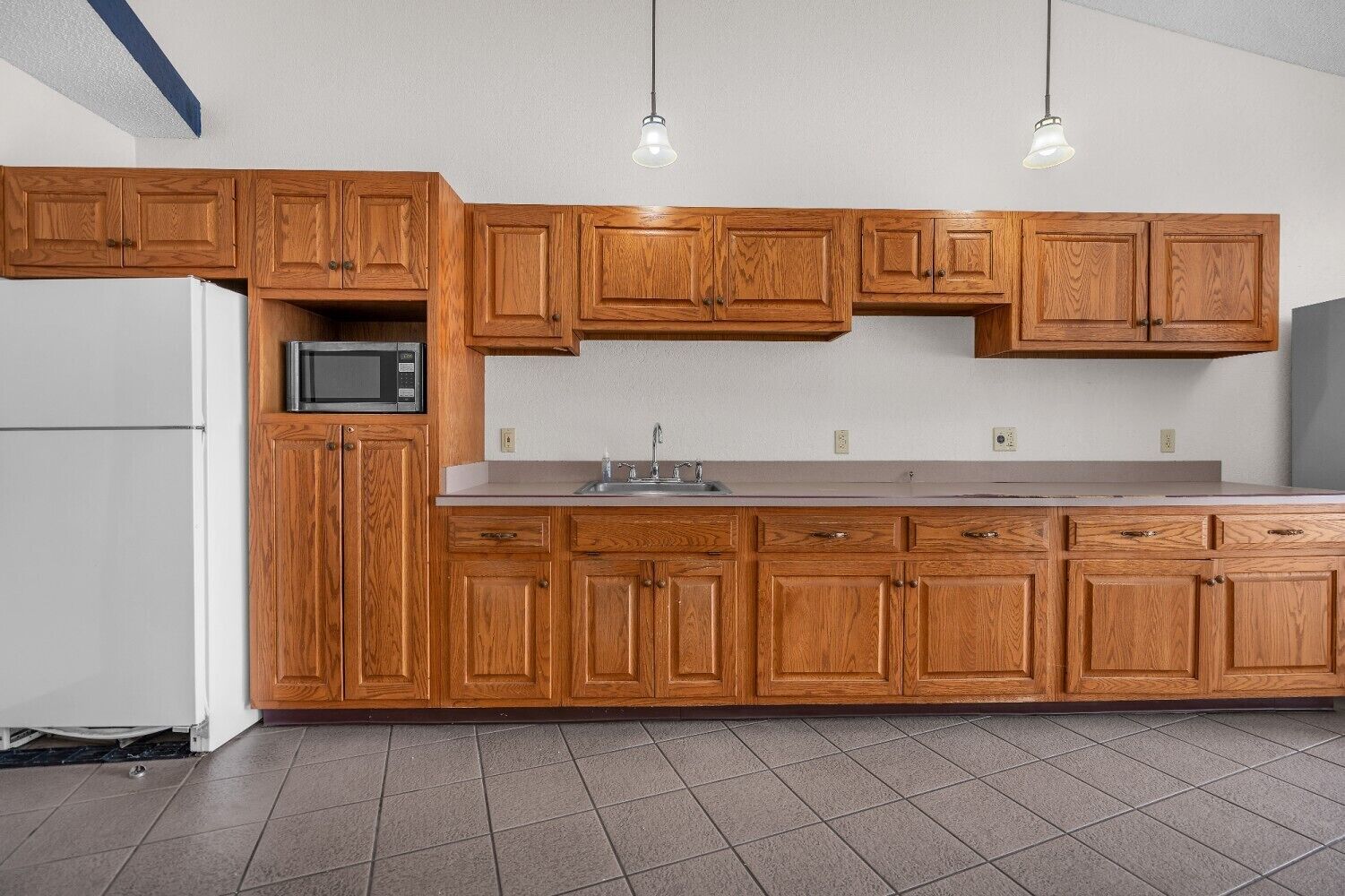 Una cocina con armarios de madera, microondas, fregadero y dos lámparas colgantes.