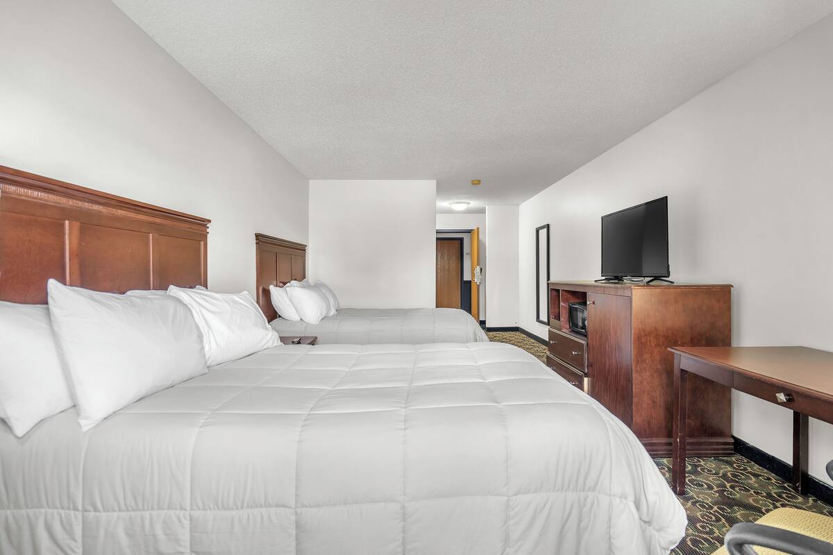 A hotel room with a large bed, a desk, a television, and a door leading to another room.